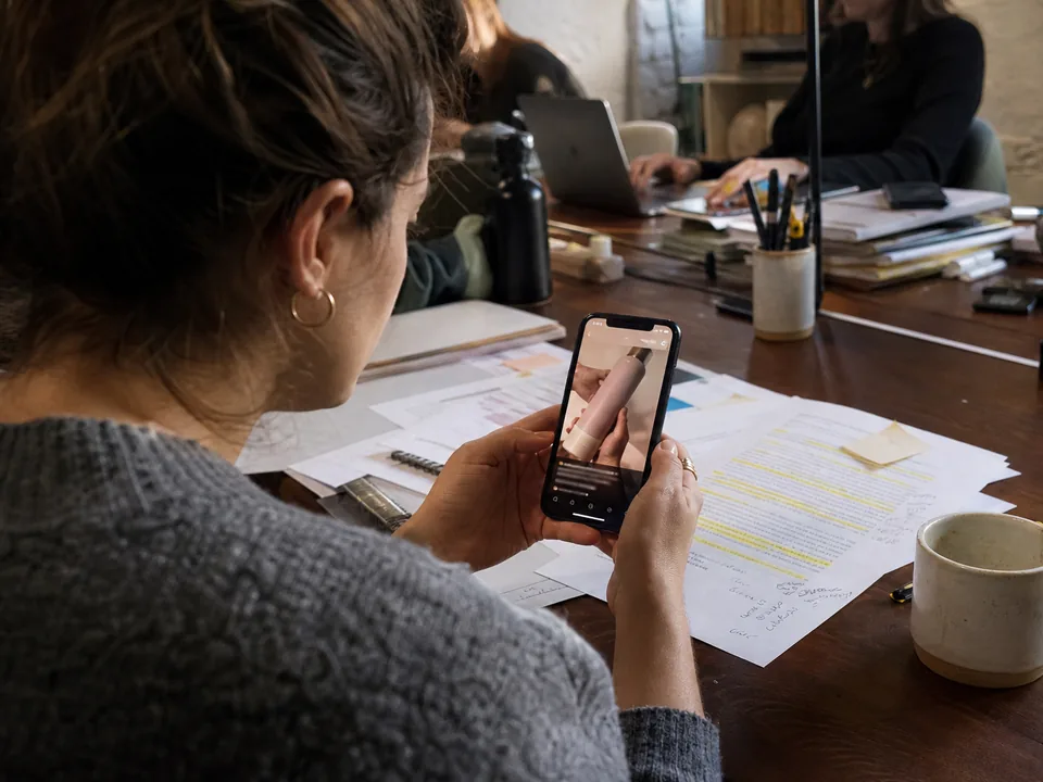 Marketer checking a vertical captioned video on a phone next to a highlighted printed blog post